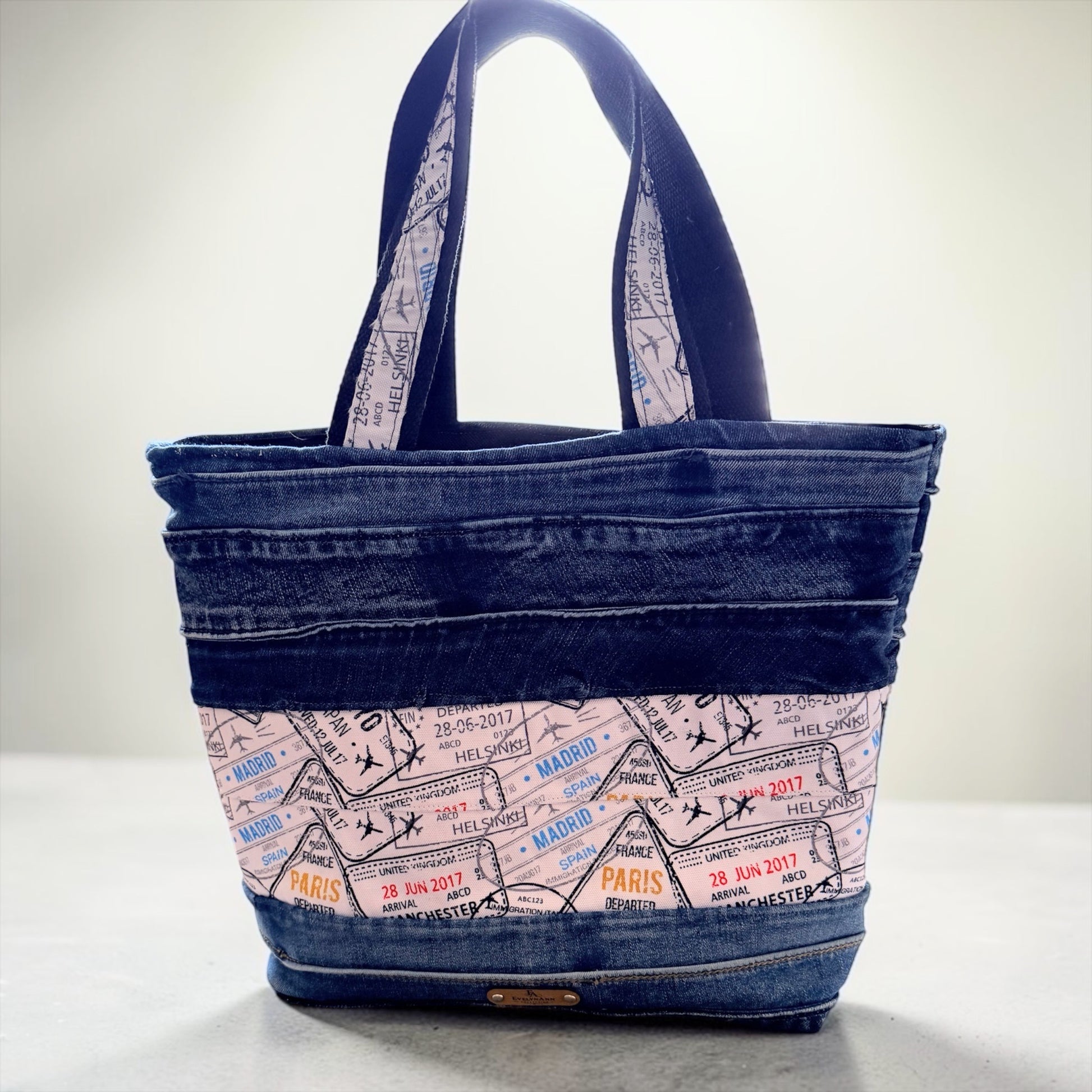 Handcrafted denim tote bag with passport stamp travel print fabric, shoulder straps, and exterior zipper pocket from the EvelynAnn™ Collection by NspiVibe.