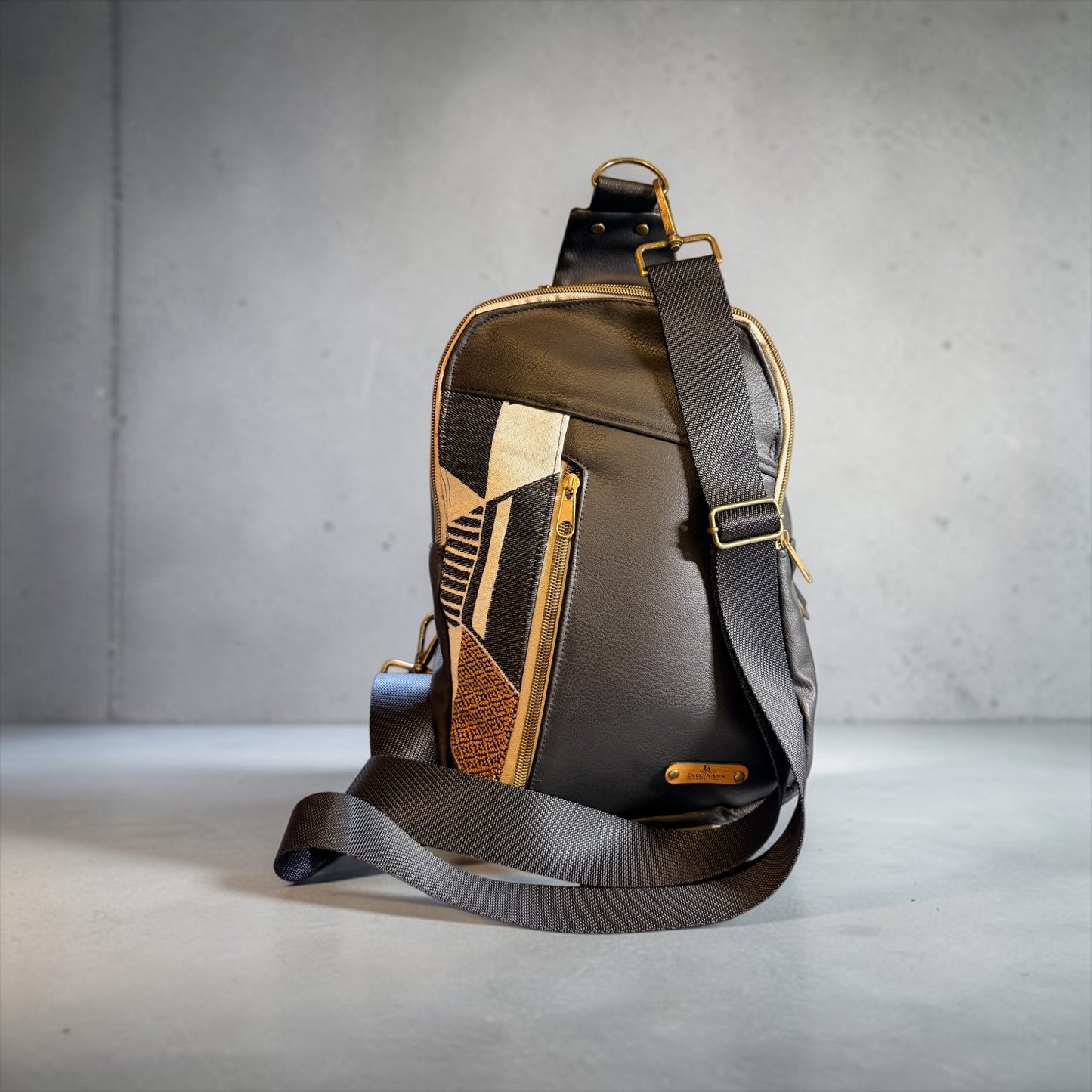 NspiVibe leather crossbody sling bag with a geometric panel, adjustable strap, and brass hardware on a grey surface.